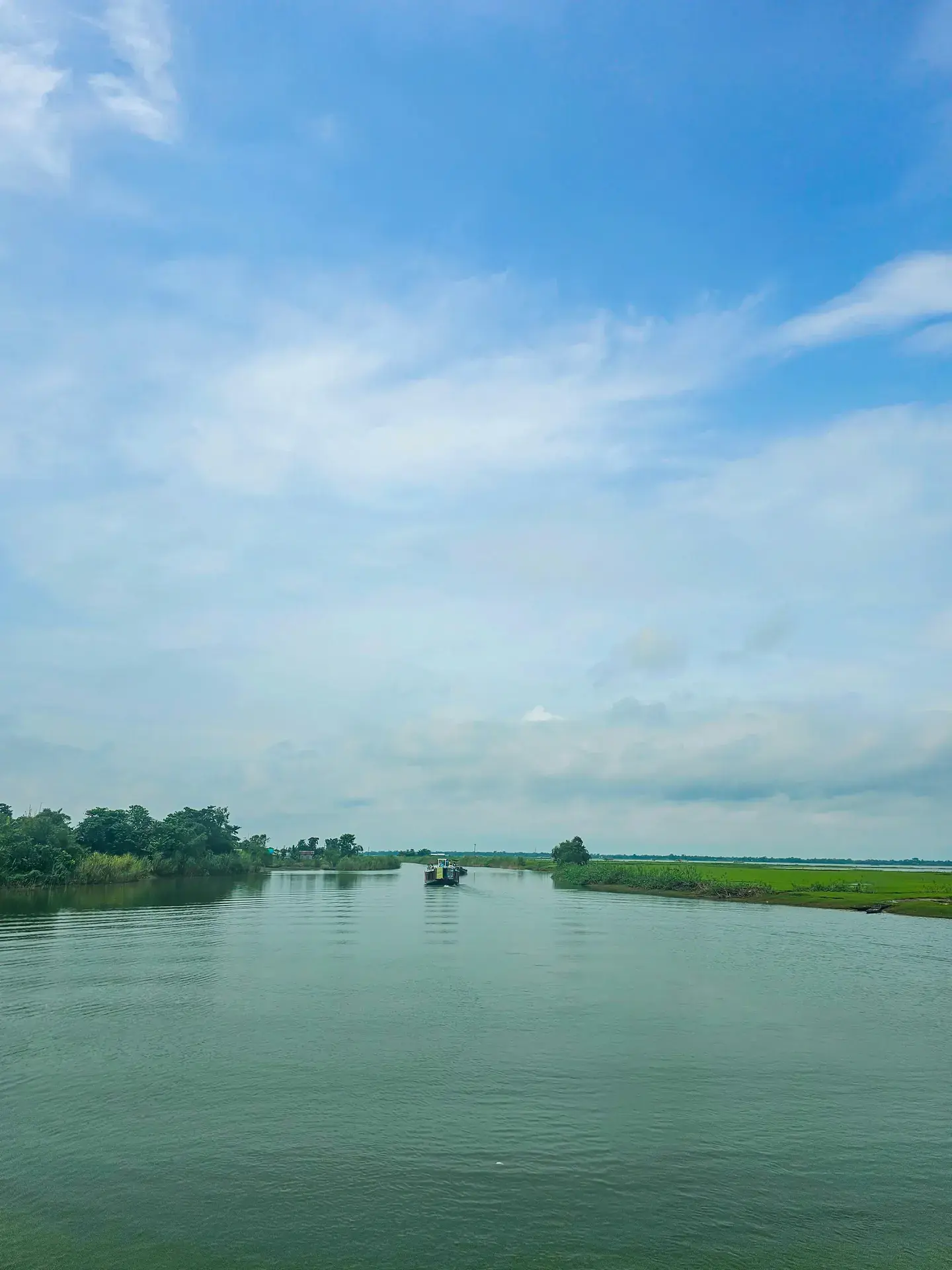 A wooden boat crossing a broad Bangladesh water landscape in soft morning light