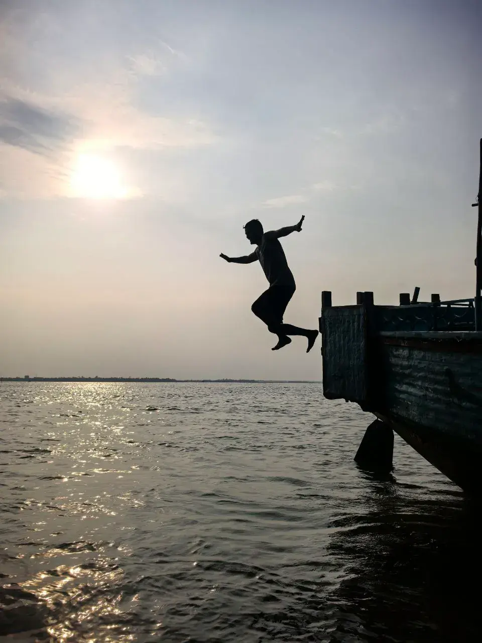 A traveler jumping from a wooden boat into open haor water at sunset